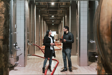 Caucasian couple walking around a winery industry production section, an impressive plant with a high ceiling and modern equipment
