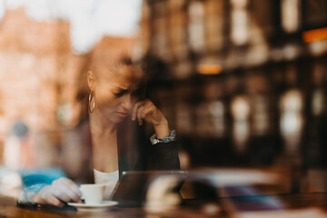 woman in a coffee shop drink coffee viewed through glass with reflections as they sit at a table chatting and laughing