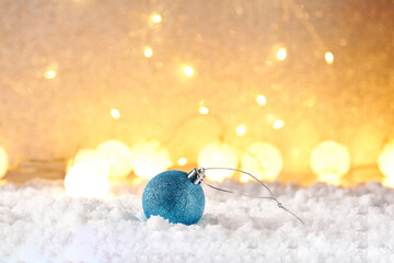 Christmas ball in the snow and christmas lights on blurred background.