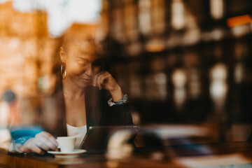 woman in a coffee shop drink coffee viewed through glass with reflections as they sit at a table chatting and laughing