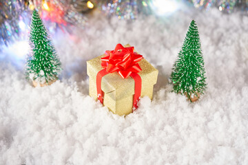 Naklejka na ściany i meble A gift box and christmas tree on snow on the background of bokeh.