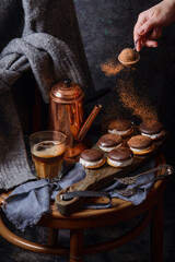 Female hand pouring with cocoa powder homemade delicious cookies. Coffee, cakes and cozy sweater in dark style as autumn season concept. Copy space