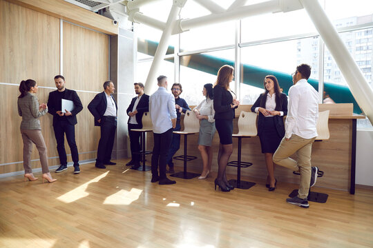 Multiracial Group Of People Gather In A Modern Office With Laminate Flooring After A Business Event Or A Corporate Team Meeting, Discuss Latest News And Talk About Work Stuff