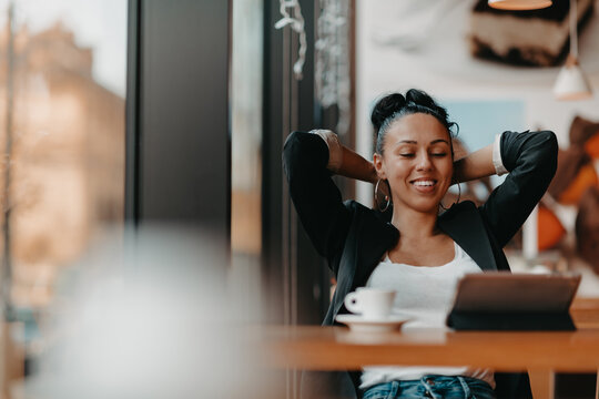 A Woman Sits In A Cafe With Her Arms Raised And Celebrating A Job Well Done.Business Concept