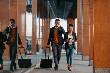 Business man and business woman talking and holding luggage traveling on a business trip, carrying fresh coffee in their hands.Business concept