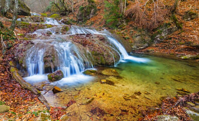 Fototapeta na wymiar small waterfall on mountain river flow through autumn mountain canyon