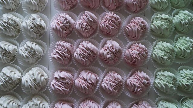 Many red, green and white cooked marshmallows lie on the table. Camera zooming
