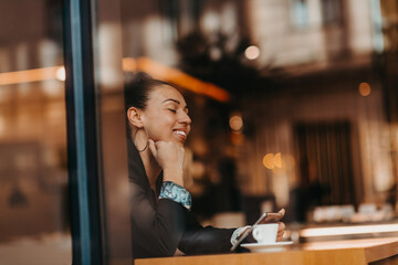 woman in a coffee shop drink coffee viewed through glass with reflections as they sit at a table chatting and laughing