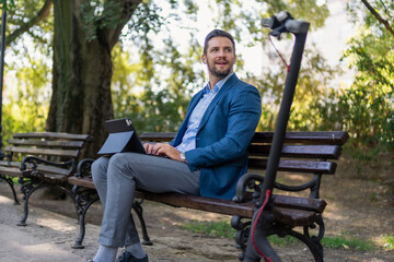 Caucasian male entrepreneur freelancer sitting outdoors in city park a bench talking online a video call using laptop or tablet. Business man office worker working on urban street background