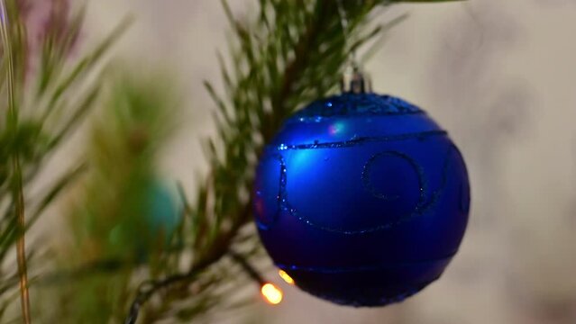 Christmas tree decorated with blue glass ball on christmas spruce branch on background bokeh of flickering light bulbs garlands. Happy New Year festival mood. Positive emotion.