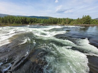 Beautiful landscape of a river with stormy waters that reflect the sky in a forest in Norway