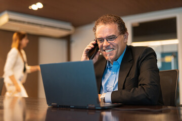 Fototapeta na wymiar Portrait of mature businessman using laptop computer and mobile phone in office horizontal shot