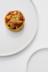 Photo of a delicious modern style handmade mini tart tartlet fulled with differ nuts like pistachio and hazelnut with salted caramel sause on a modern porcelain white flat plate on white background