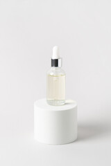 Facial serum in glass dropper bottle on white podium on light grey background. Natural skin care...