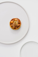 Photo of a delicious modern style handmade mini tart tartlet fulled with differ nuts like pistachio and hazelnut with salted caramel sause on a modern porcelain white flat plate on white background