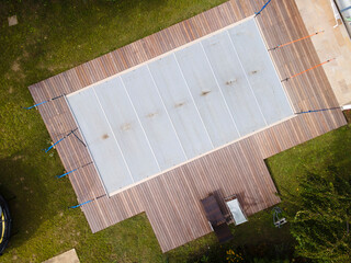 Drone photo of pool which is covered with grey pool tarpaulin, cover and prepared for winter and a garden with house