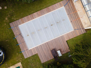Drone photo of pool which is covered with grey pool tarpaulin, cover and prepared for winter and a garden with house