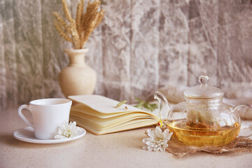 Herbal linden tea in teapot with cup of tea. Wheat,flowers, autumn decorations and notebook. Cozy atmosphere relax at home.
