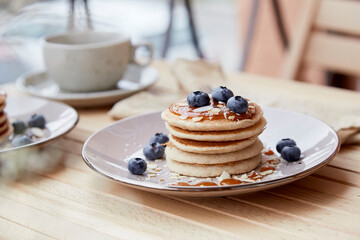 Tasty traditionalvegan pancakes with fresh blueberries and agave syrup on a plate. Cup of coffee on background. Breakfast outside