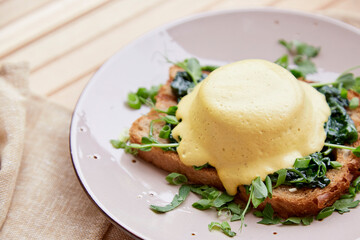 Vegan eggs benedict dish with wholegrain bread, smoked tofu, young onion, parsley, greens, pea sprouts outside.