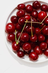 Obraz na płótnie Canvas Photo of many fresh and juicy cherry berries on a flat white porcelain plate close up on a white background