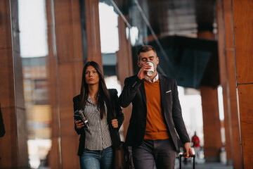 Fototapeta premium Business man and business woman talking and holding luggage traveling on a business trip, carrying fresh coffee in their hands.Business concept