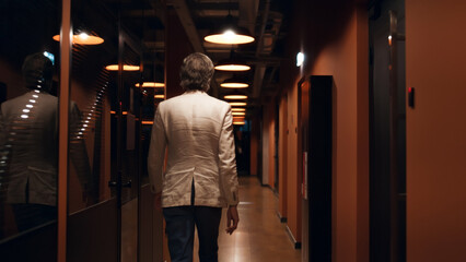 Back view of successful businessman in suit walking in modern corridor. Male office worker going to work. Office hallway of E-commerce marketing company
