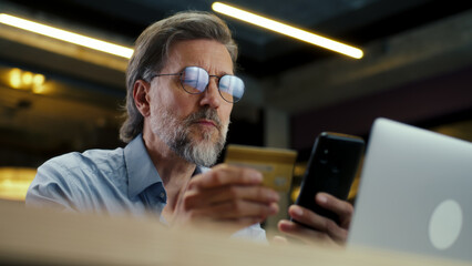 Businessman using phone, transferring money on bank card, paying for service online during work in modern office of marketing company. E-commerce business center
