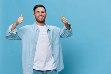 Fototapeta premium Enjoyed friendly tanned handsome man in casual basic t-shirt show thumbs up gesture Like posing isolated on blue studio background. Copy space Banner Mockup. People emotions Lifestyle concept