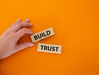 Build trust symbol. Wooden blocks with words Build trust. Beautiful orange background. Businessman hand. Business and Build trust concept. Copy space.