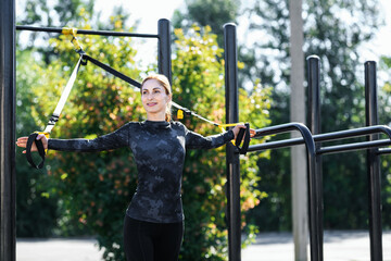 Women and sport. Smiling girl in sportswear with sports equipment TRX exercising outdoors at the gym. Middle aged sportswoman