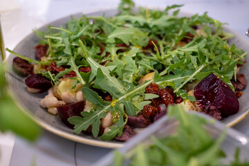 
Gray plate with salad of arugula, beets, Greek cheese on a white kitchen table. Healthy vegetarian food.