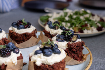 Fototapeta na wymiar brownie muffins with cream and blueberries on a plate. A plate of healthy green salad on a blurred background
