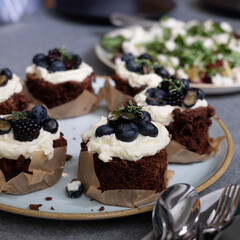 brownie muffins with cream and blueberries on a plate. A plate of healthy green salad on a blurred background
