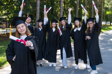 Happy young caucasian woman celebrating graduation with classmates. A group of graduate students outdoors.