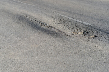 Broken road with holes and cracks built in countryside on hot sunny day. Deformed and expanded asphalt surface with potholes caused by heavy overloaded trucks driving on highway at rural site closeup
