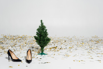 elegant and black high heeled shoes near green christmas tree and sparkling confetti on grey background