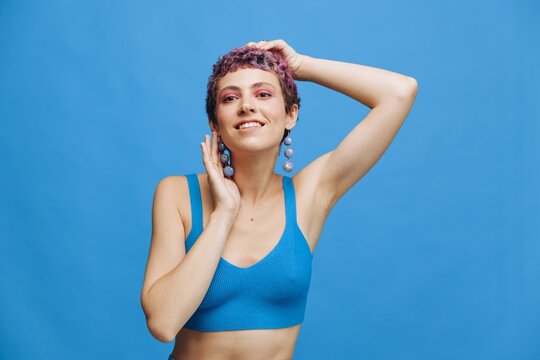 Young athletic fashion woman with colored hair and short haircut posing and dancing in blue sportswear smiling and looking at the camera on a blue monochrome background