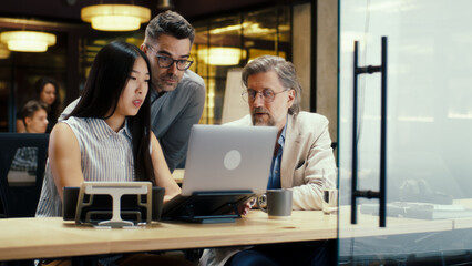 Diverse creative office workers talking and having working conference in modern office, using laptop and digital tablet. Businesspeople working on startup project. Discussion of company strategy