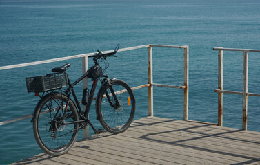 Fototapeta premium End of a bike trip. black modern bicycle with plastic box and bottle of water on a wooden pier over Caspian Sea water. Aktau, kazakhstan
