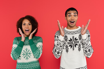 amazed african american couple in warm sweaters looking at camera and showing wow gesture isolated...