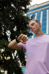 A handsome guy in denim shorts and a pink t-shirt poses beautifully in the city