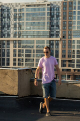 A handsome guy in denim shorts and a pink t-shirt poses beautifully in the city