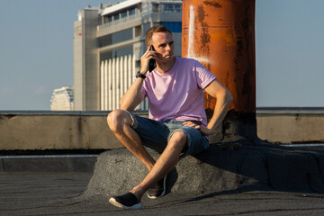 Fototapeta na wymiar A handsome guy in denim shorts and a pink t-shirt poses beautifully in the city