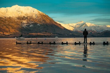 Landscape view of the sunrise over the Wanaka lake surrounded by mountains. A man is standing