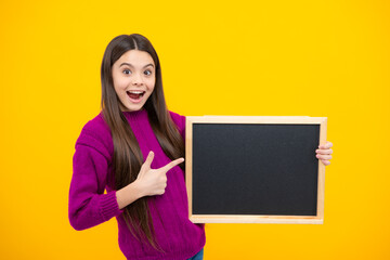 Teenager younf school girl holding school empty blackboard isolated on yellow background. Portrait of a teen female student. Copy space, mockup advertisement.