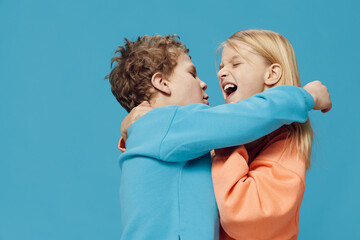 cute, joyful, loving children of school age stand on a blue background and gently hug each other.