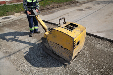 Worker use vibratory plate compactor compacting gravel at road construction site