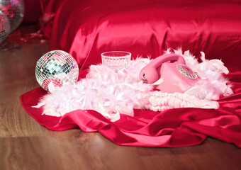 Pink old telephone, white feathers, disco ball, lie on floor near bed. Glamor party.