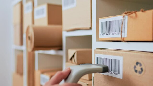 An employee of a postal company scans a barcode on a cardboard box, entering data on sending a parcel to the database of sending parcels to customers, accounting for parcel boxes in a warehouse
